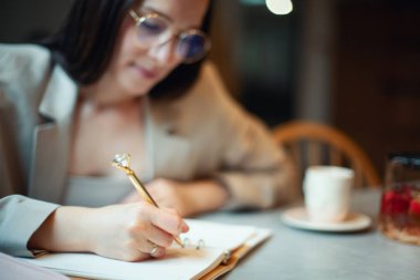 Koyu renk takım elbiseli, genç ve güzel bir kadın tatil zamanında kahve içerken iş planlarını günlüğe yazıyor. Planlama ve zaman yönetimi konsepti. Olumlu bir tavırla öğrenmek.