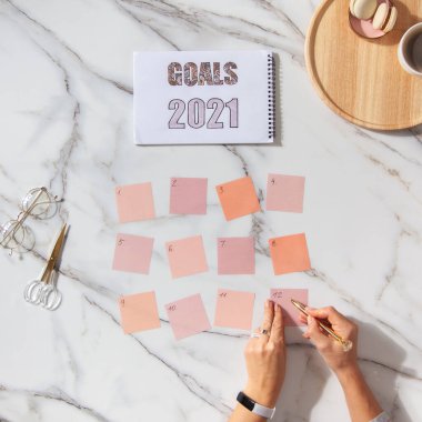 Top view of well groomed female hands near stack of colorful notepads for writing goals and plans for future New Year 2021. Pile of clean notes papers on coral colored background with copy space. clipart