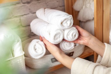 Sıcak bornozlu kadın, beyaz tuğla duvara sarılı, çarşaflar, battaniyeler, yorganlar ve vazo ile birlikte ahşap çarşaf dolabına rulo pamuklu banyo havluları koyuyor. Marie Kondo yöntemi.