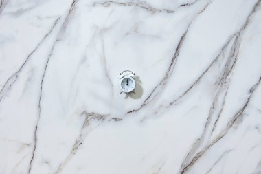 Beyaz mermer arka planda gece yarısı ya da 12 'yi gösteren beyaz alarmlı saatin üst görüntüsü. 2021 yılbaşı ve Noel arifesi kartları kavramı. Bayram kutlaması..