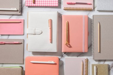 Beyaz mercan, gri renkli günlük veya beyaz mermer zemin üzerinde not defterleri ve kalemler bulunan yaratıcı düz çalışma masası. Planlar ve hedefler yazmak için kırtasiye malzemesi kullanma kavramı.