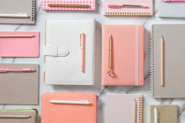 Beyaz mercan, gri renkli günlük veya beyaz mermer zemin üzerinde not defterleri ve kalemler bulunan yaratıcı düz çalışma masası. Planlar ve hedefler yazmak için kırtasiye malzemesi kullanma kavramı.