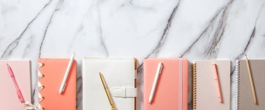 Beyaz mercan, gri renkli günlük veya beyaz mermer zemin üzerinde not defterleri ve kalemler bulunan yaratıcı düz çalışma masası. Planlar ve hedefler yazmak için kırtasiye malzemesi kullanma kavramı.