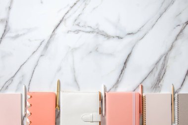 Beyaz mercan, gri renkli günlük veya beyaz mermer zemin üzerinde not defterleri ve kalemler bulunan yaratıcı düz çalışma masası. Planlar ve hedefler yazmak için kırtasiye malzemesi kullanma kavramı.