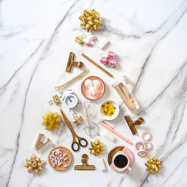 Вид сверху творческой формы елки из канцелярских принадлежностей, будильника, элементов елочного украшения и кофе с зефиром с копировальным пространством на белом мраморном фоне. Праздничные дни
