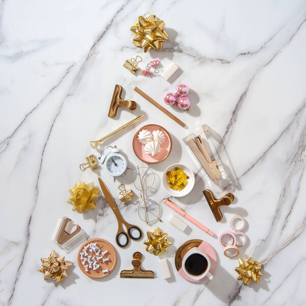 Вид сверху творческой формы елки из канцелярских принадлежностей, будильника, элементов елочного украшения и кофе с зефиром с копировальным пространством на белом мраморном фоне. Праздничные дни