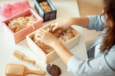 Genç bir kadın, el yapımı organik sabunlar, banyo tuzu, fırçalı sünger ve banyo bombalarını nedime hediye seti içine yerleştiriyor. Kadınların gününü güzelleştirmek için hediye kutuları..