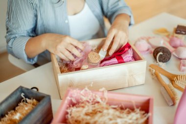 Genç bir kadın, el yapımı organik sabunlar, banyo tuzu, fırçalı sünger ve banyo bombalarını nedime hediye seti içine yerleştiriyor. Kadınların gününü güzelleştirmek için hediye kutuları..