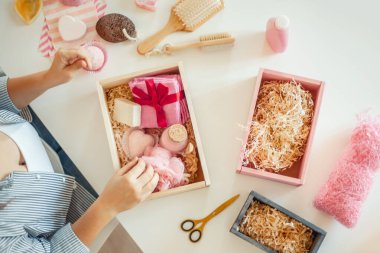 Genç bir kadın, el yapımı organik sabunlar, banyo tuzu, fırçalı sünger ve banyo bombalarını nedime hediye seti içine yerleştiriyor. Kadınların gününü güzelleştirmek için hediye kutuları..