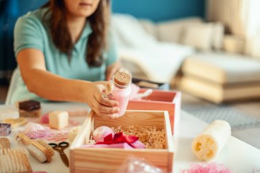 Genç bir kadın, el yapımı organik sabunlar, banyo tuzu, fırçalı sünger ve banyo bombalarını nedime hediye seti içine yerleştiriyor. Kadınların gününü güzelleştirmek için hediye kutuları..