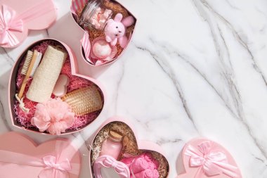 Pembe renkli kalp şekilli hediye kutularının üst görüntüsü ev yapımı banyo malzemeleri, lokum ve beyaz mermer arka plandaki kadınlar için vücut bakım ürünleri. Noel hediyeleri kavramı.