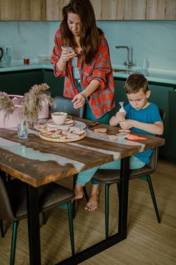 Çocuk annesi için bir sürpriz hazırlıyor. Kurabiyeleri kalp şeklinde pembe kremayla süslüyor. Aşk konsepti.