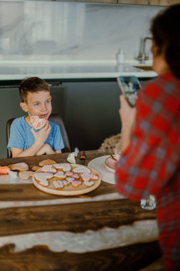 Çocuk annesi için bir sürpriz hazırlıyor. Kurabiyeleri kalp şeklinde pembe kremayla süslüyor. Aşk konsepti.