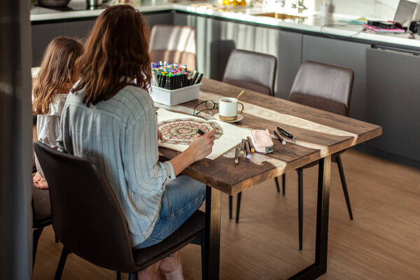 Mom and daughter are doing Zen painting together in their home in the kitchen. Concept for meditation, doodle drawing and hobbies.