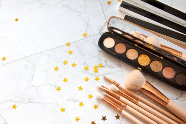 Dekoratif kozmetik göz falı paleti ve beyaz mermer masa üzerinde altın yıldız şekilli konfeti ile farklı boyutlarda makyaj fırçası düz bir bileşim yatıyordu. Güzellik ve moda konsepti. Boşluğu kopyala.