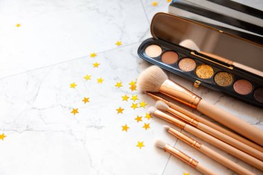 Dekoratif kozmetik göz falı paleti ve beyaz mermer masa üzerinde altın yıldız şekilli konfeti ile farklı boyutlarda makyaj fırçası düz bir bileşim yatıyordu. Güzellik ve moda konsepti. Boşluğu kopyala.