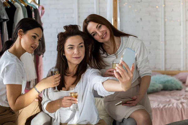 自宅パーティーでスマホを使って一緒にポーズをとる3人の女性友達のグループ 幸せな女性作る自撮り上の携帯電話で楽しい飲み物シャンパンで家の寝室のインテリア — ストック写真
