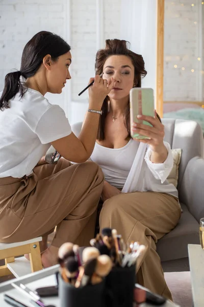 女性のヴィジターは 自宅で準備を取得する女性クライアントに化粧化粧品を適用します アーティストの作業染料手順を構成します 2人の女性の友人一緒に時間を過ごす準備でワードローブの部屋 — ストック写真
