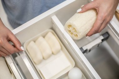 Kadın ellerinin temiz bir şekilde banyo konforu ve tuvalet malzemelerini çekmeceye ya da banyodaki dolaba yerleştirmesi. Marie Kondo 'nun yöntemini kullanarak bir banyo deposunu toparlama fikri.