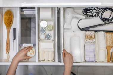 Kadın ellerinin temiz bir şekilde banyo konforu ve tuvalet malzemelerini çekmeceye ya da banyodaki dolaba yerleştirmesi. Marie Kondo 'nun yöntemini kullanarak bir banyo deposunu toparlama fikri.