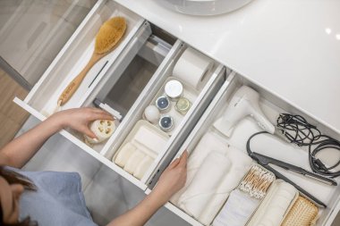 Kadın ellerinin temiz bir şekilde banyo konforu ve tuvalet malzemelerini çekmeceye ya da banyodaki dolaba yerleştirmesi. Marie Kondo 'nun yöntemini kullanarak bir banyo deposunu toparlama fikri.