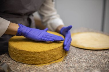 Gülümseyen kadın pastacı yemek servisi restoranında çalışan bisküvi şeklindeki kekin üzerine çikolatalı gommage döküyor. Üniformalı kadın aşçı kremalı tatlı hazırlıyor.