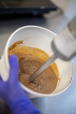 Kendine güvenen kadın pastacı karışımı mutfak yemeklerinde tatlı hamur işi hazırlamak için blender kullanır. Üniformalı kadın aşçı tatlı kreması ya da hamuru kasede hazırlıyor.