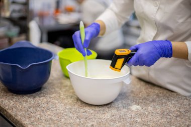 Çikolata sıcaklığı ölçen tatlı pişiren profesyonel kadın pastacının yakın çekim elleri. Pastanenin mutfağındaki kaseye karıştırılmış tatlı ve lezzetli yemek hazırlama süreci.