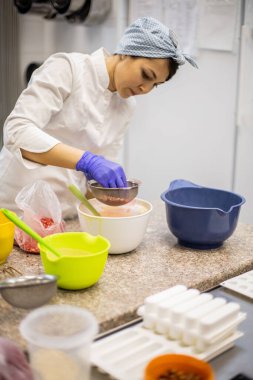 Kendine güvenen mutfak çalışanı kadın kremalı çikolatalı tart süslemek için elek aracılığıyla çilek tozu sürüyor. Meşgul kadın aşçı aşçılıkta pasta için lezzetli dekorlar pişiriyor.