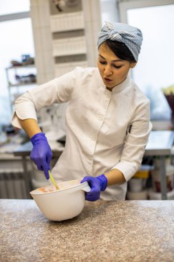 Kendine güvenen mutfak çalışanı kadın kremalı çikolatalı tart süslemek için elek aracılığıyla çilek tozu sürüyor. Meşgul kadın aşçı aşçılıkta pasta için lezzetli dekorlar pişiriyor.