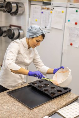 Kadın pastacı, hamur işi pişirmek için plastik kalıba çikolata döküyor. Üniformalı kadın aşçı, pastane mutfağında çalışarak lezzetli bir tatlı hazırlıyor.