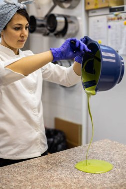 Üniformalı kadın pastacı mutfaktaki kaseden tabağa sıvı kibrit çay çikolatası döküyor. Bayan mutfak personeli tatlı şekerlemeler için yemek pişiriyor pastanede lezzetli pastalar yapıyor.