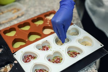 Kauçuk kalıpta kibrit çayla çikolata pişiren, böğürtlen şekeri dekoru uygulayan eldiven giymiş yakın çekim elleri. Pastanede ya da pastanede lezzetli bir tatlı hazırlıyorum.