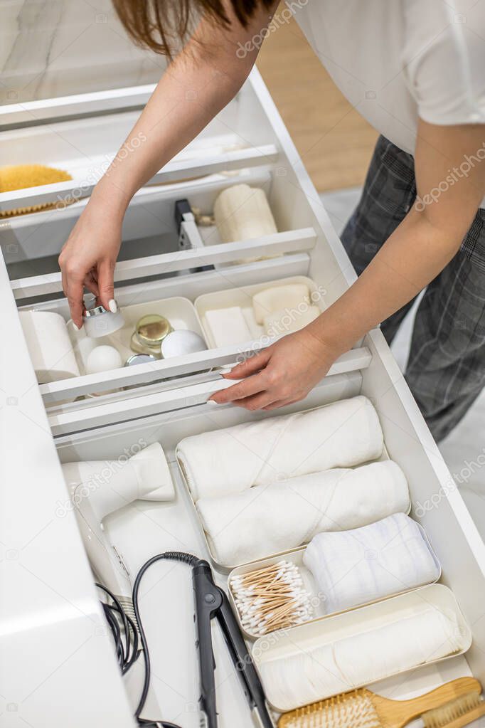 Young woman organizing bathroom storage, displaying beauty cosmetic creams and toiletries into drawer with dividers. Bathroom vanity decluttering concept by using KonMari method.