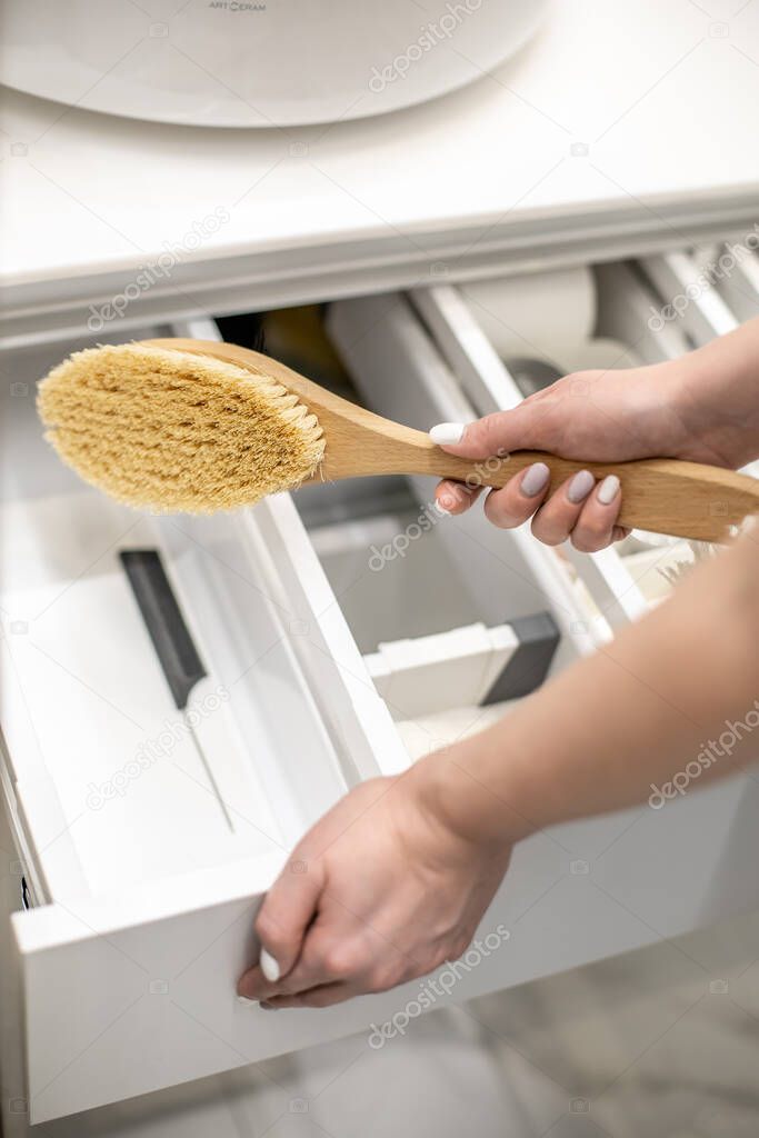 Happy young woman is holding wooden brush and putting into the drawer together with bathroom amenities. Housewife is organizing bathroom storage. Konmari method of bathroom declutter. Copy space.