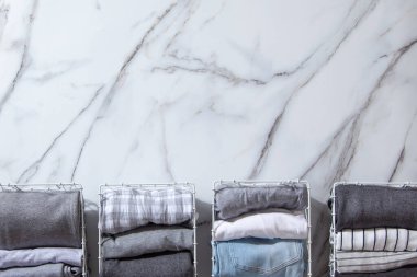Beyaz mermer masaya konmuş organik pamuklu pijama grubu katlanıp beyaz çelik tel örgü sepetlere yerleştirilmeye hazır. Dolap düzenleme konsepti. İskandinav tarzı renkler. Konmari yöntemi kullanılıyor.