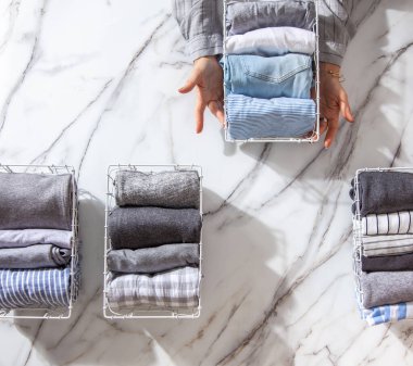 Beyaz mermer masanın üzerindeki metal ağ düzenleyici sepetinde düzgün katlanmış giysiler ve pijamalar. Marie Kondo giyim tarzı konsepti düşürür ve sınıflandırır. Ev hanımı Konmari 'nin temizlik yöntemini kullanıyor..