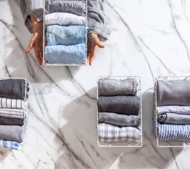 Beyaz mermer masanın üzerindeki metal ağ düzenleyici sepetinde düzgün katlanmış giysiler ve pijamalar. Marie Kondo giyim tarzı konsepti düşürür ve sınıflandırır. Ev hanımı Konmari 'nin temizlik yöntemini kullanıyor..