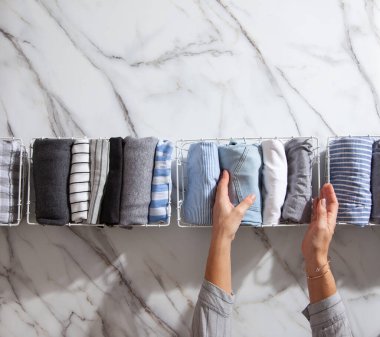 Beyaz mermer masanın üzerindeki metal ağ düzenleyici sepetinde düzgün katlanmış giysiler ve pijamalar. Marie Kondo giyim tarzı konsepti düşürür ve sınıflandırır. Ev hanımı Konmari 'nin temizlik yöntemini kullanıyor..