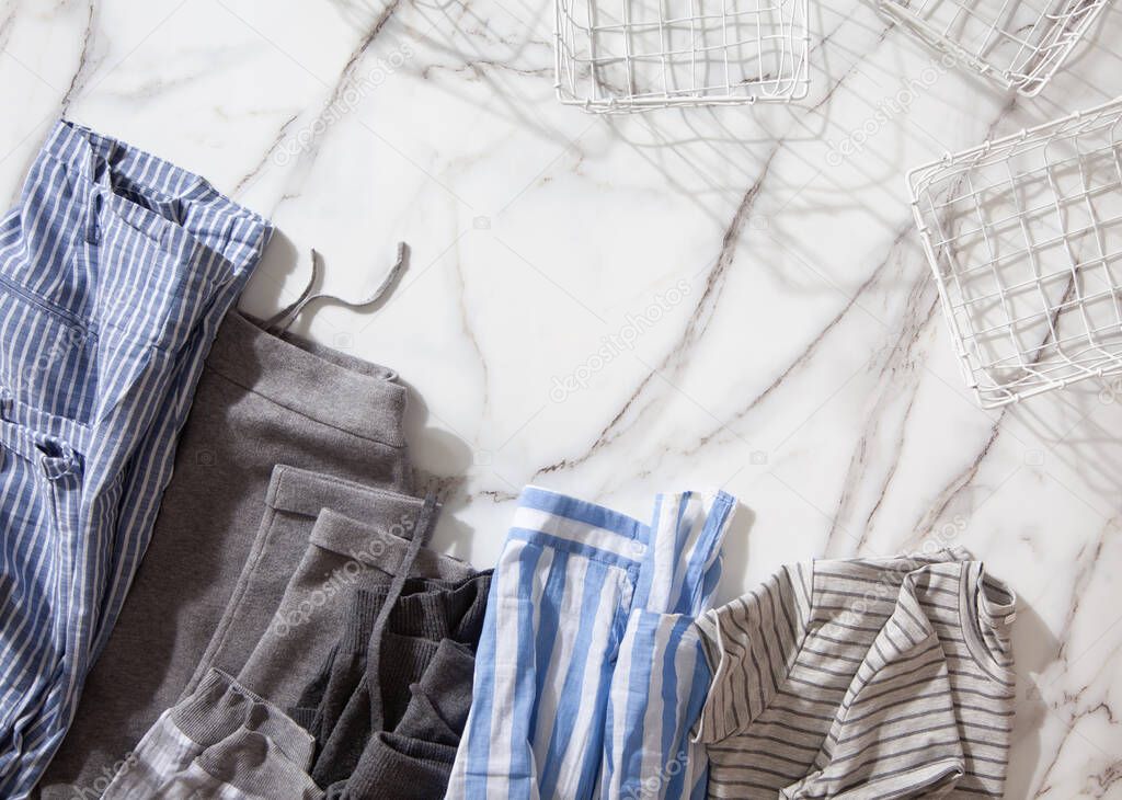Group of organic cotton pyjamas set on white marble table is ready for folding and placing into white steel wire mesh baskets. Closet organizing concept. Nordic style colors. Using konmari method.