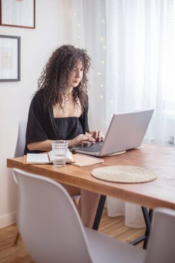 Kıvırcık esmer, serbest çalışan kadın ev yapımı İskandinav iç mekanında uzaktan kumanda kullanıyor. Modern kadın internette sohbet ediyor. İnternetten alışveriş yapıyor. Evraklar rahat bir dairede.