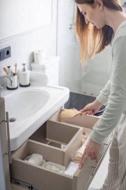 Üst düzey kadın ev hanımı lavabonun altındaki açık çekmeceye tuvalet ve tuvalet malzemeleri koyuyor. Ev işlerinden hoşlanan bir kadın Marie Kondo 'nun yöntemini kullanıyor. Modern alan düzenleme iç mimarisi