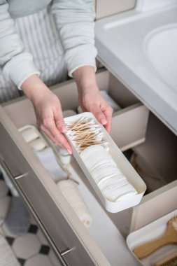 Ev hanımı elleri havluyu lavabonun altındaki açık çekmeceye koyuyor. Banyo manzarasında depolama alanı düzenleyen bir kadın. Kadın evde temizlik yapıyor. Modern Marie Kondo 'nun metodu