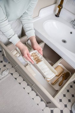 Housewife hands putting rolled up towel into open drawer under sink. Female organizing storage space in bathroom top view. Woman cleaning housework at home. Modern Marie Kondo's keeping method clipart