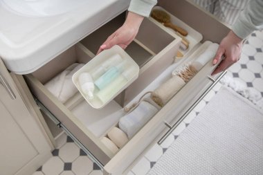 Ev hanımı elleri havluyu lavabonun altındaki açık çekmeceye koyuyor. Banyo manzarasında depolama alanı düzenleyen bir kadın. Kadın evde temizlik yapıyor. Modern Marie Kondo 'nun metodu