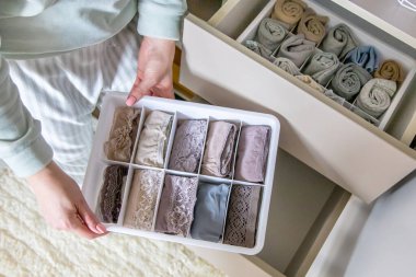 Üst düzey kadın eller, Marie Kondo 'nun metoduyla birlikte düzenleyici çekmece ayırıcıyı tutuyor. Ev hanımı kolları gardırop dolabını düzenliyor. Modern kadın katlanmış giysiler için konteynır kullanıyor