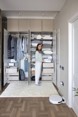 Neşeli ev kadını dolapta kutu yerleştiriyor gardıropta ev işlerinin keyfini çıkarıyor. Mutlu ev hanımı rahat evdeki dolabı düzenliyor. Pijamalı gülümseyen kadın elbiselerini düzenliyor.