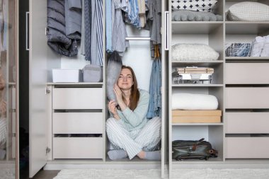 Pijamalı gülümseyen ev hanımı gardıropta yastıkta uyuyor. Modern dolabın içinde kıyafetlerle saklanan eğlenceli, genç bir kadın. Memnuniyet verici ev hanımı hafta sonu evde eğleniyor.
