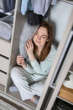 Pijamalı gülümseyen ev hanımı gardıropta yastıkta uyuyor. Modern dolabın içinde kıyafetlerle saklanan eğlenceli, genç bir kadın. Memnuniyet verici ev hanımı hafta sonu evde eğleniyor.