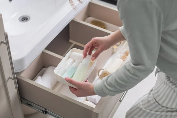 Üst düzey kadın ev hanımı lavabonun altındaki açık çekmeceye tuvalet ve tuvalet malzemeleri koyuyor. Ev işlerinden hoşlanan bir kadın Marie Kondo 'nun yöntemini kullanıyor. Modern alan düzenleme iç mimarisi